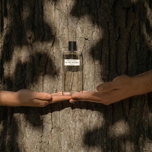 Fles In the Woods Eau de Parfum in handen, voor een boomschors.