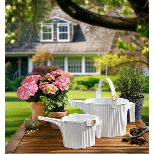 Twee gieters in wit en bloemen op een tafel in de tuin