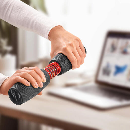 Persoon traint met een pols- en onderarmtrainer aan een tafel met laptop.