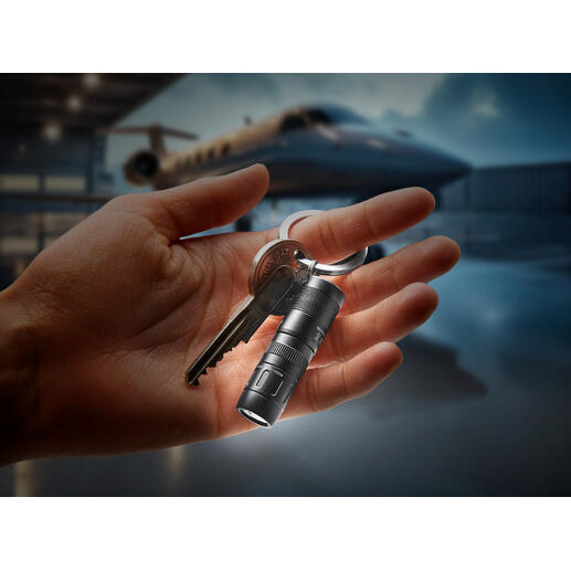 Hand houdt magnetische mini-zaklamp met sleutelring vast, licht straalt in het donker.