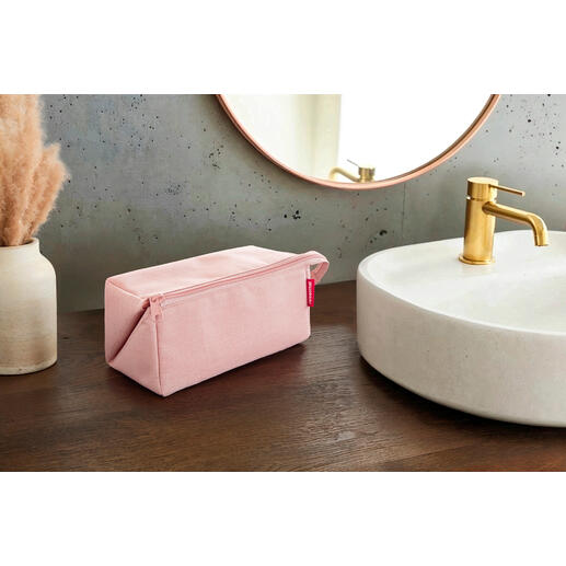 Roze 2-in-1 reisnecessaire op een houten tafel naast een wastafel