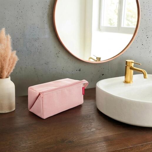 Roze 2-in-1 reisnecessaire op een houten tafel naast een wastafel