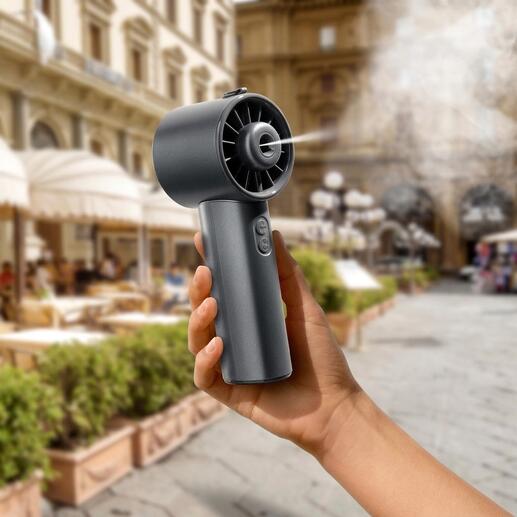 Hand houdt een Hydro-Mini-ventilator in een stad, met historische gebouwen op de achtergrond.