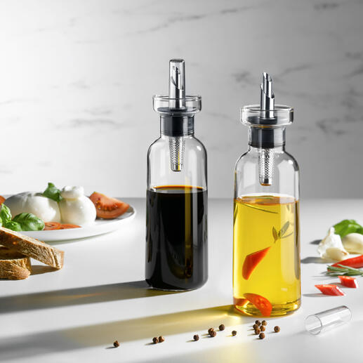 Olie- en azijnspuiter-set met decoratieve schenker en verse ingrediënten op een tafel.