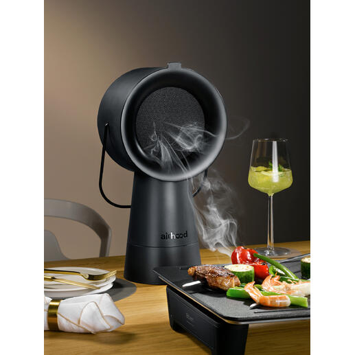 Airhood 2.0 in het zwart, rokend grillapparaat op tafel met groenten en vlees.