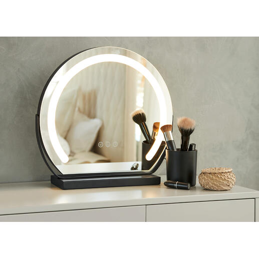 Ronde make-up spiegel met verlichting op een tafel, omringd door cosmetica accessoires.