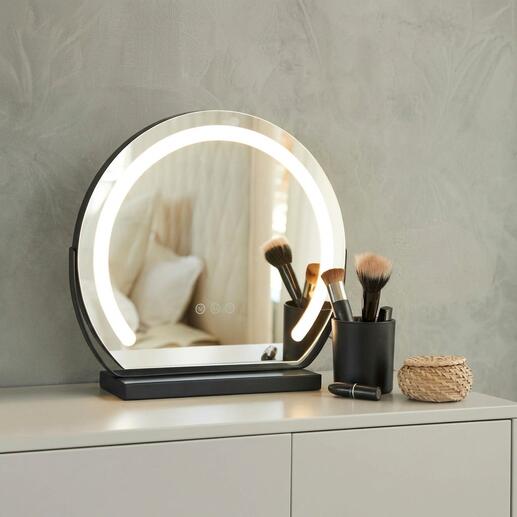Ronde make-up spiegel met verlichting op een tafel, omringd door cosmetica accessoires.