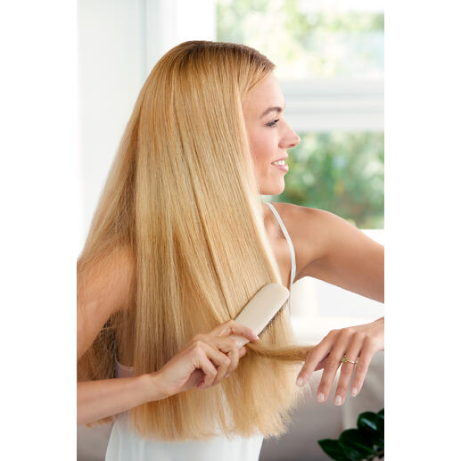Vrouw met blond haar borstelt haar haar met een haarborstel op een lichte achtergrond.