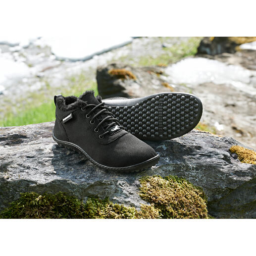 Zwarte winter sneakers op een steen met sneeuwresten op de achtergrond.