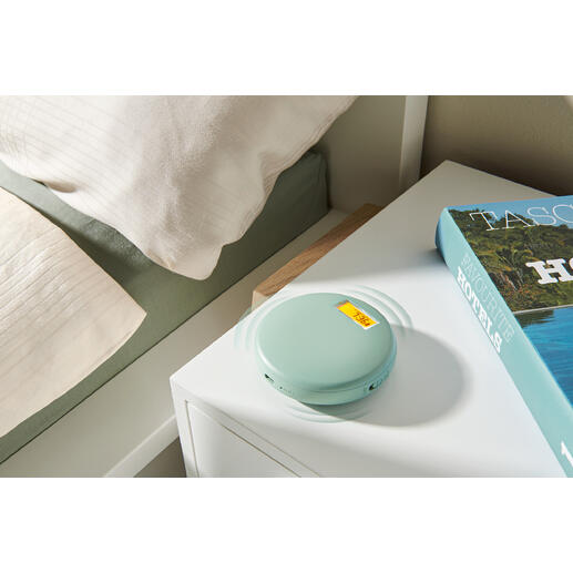 Vibratiewekker in zachtgroen, op een nachtkastje naast een boek en een dekbed.