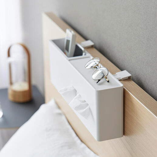 Witte tissuebox aan het hoofdeinde van een bed met bril en smartphone.