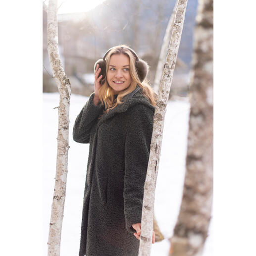 Vrouw met alpaca oorkappen staat voor berken in de sneeuw.