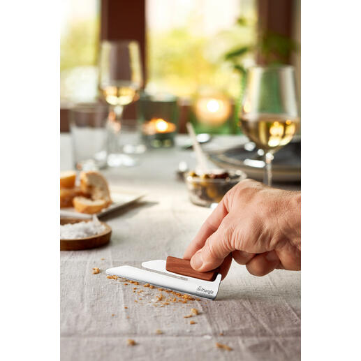 Hand laat de design kruimelvanger zien op een gedekte tafel met snacks.