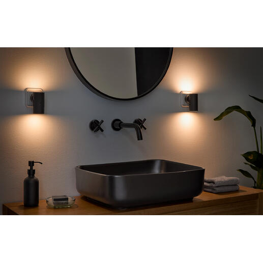 Dimbare wandlamp in een badkameromgeving naast een moderne wastafel.