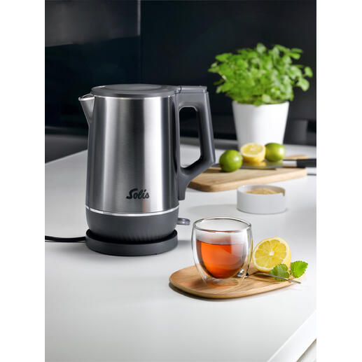 Dubbele waterkoker met roestvrijstalen afwerking en thee in glazen kom op tafel.