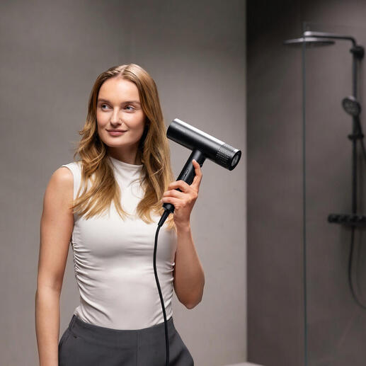 Vrouw houdt een zwarte föhn vast in een moderne badkamer.