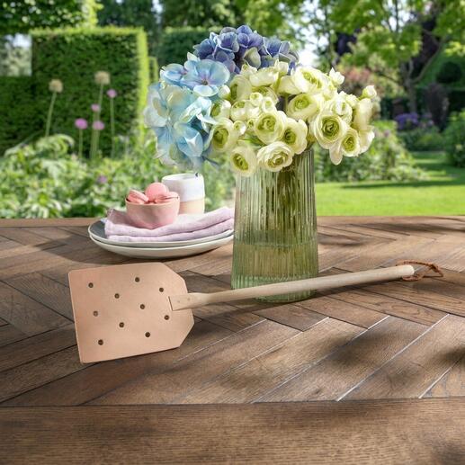 Leren vliegenmepper ligt decoratief op een rustieke houten tafel.