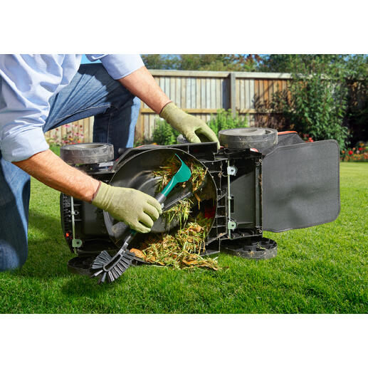 Persoon maakt een omgedraaide grasmaaier schoon met een gereedschap terwijl grasresten worden verwijderd.