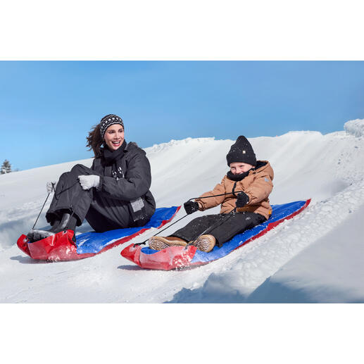 Vrouw en kind glijden van een sneeuwhelling met XL-sleetjes.