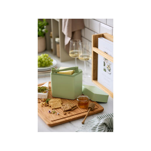 Kaas vershoudbox met snijder op een houten snijplank naast crackers en honing.