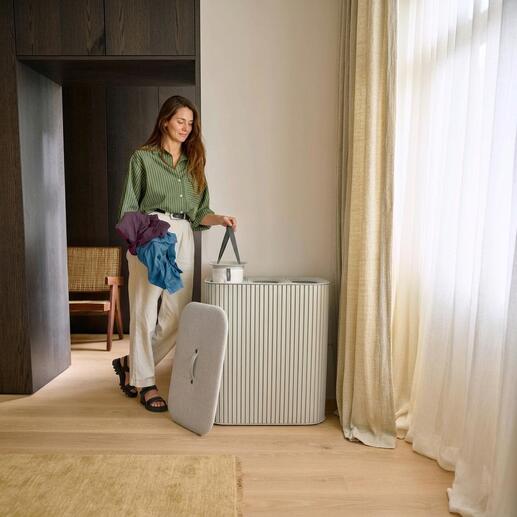 Vrouw met kleurrijke kledingstukken staat naast een wasverzamelaar.