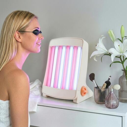 Gezichtsbruiner met roze en blauwe lampen, staat op een tafel naast cosmetica.
