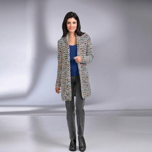 Vrouw in meerkleurige gebreide cardigan staat glimlachend.