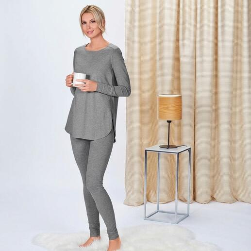 Vrouw in grijs longsleeve en sweatpants houdt een beker vast, staand in een moderne ruimte.