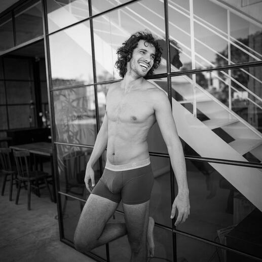 Man in boxershorts, glimlachend voor een glazen wand.