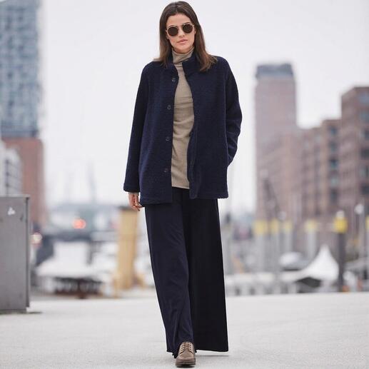 Vrouw in een donkerblauwe outfit met een gebreide jas en brede broek in een winterse stadslandschap.