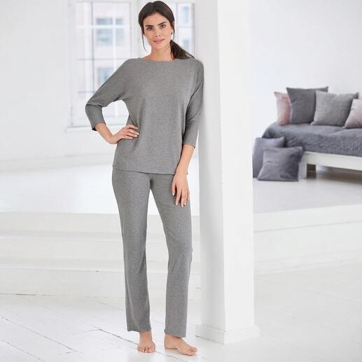 Vrouw in grijze homewear 3-delige set staat tegen een muur.