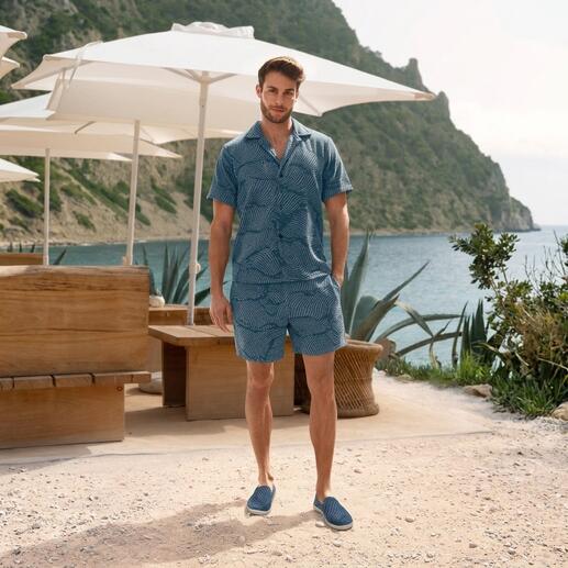 Man in gestreept Terry-shirt en korte broek staat op het strand
