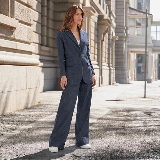 Vrouw in denimlook-pak met een ruime snit, staat in een stedelijke omgeving.