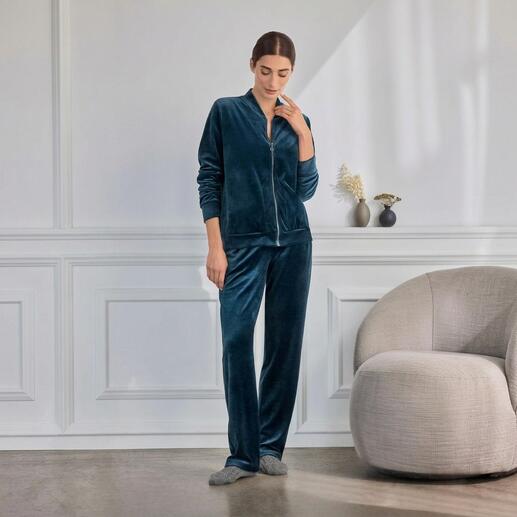 Vrouw draagt een groene Hanro loungevelours pak, ontspannen in een moderne omgeving.