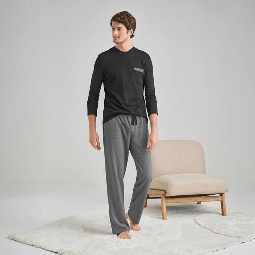 Man in zwart t-shirt met lange mouwen en grijze pyjamabroek staat op een tapijt.