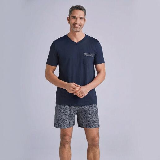 Man in een marineblauw T-shirt en grijze shorts, glimlachend voor een neutrale achtergrond.