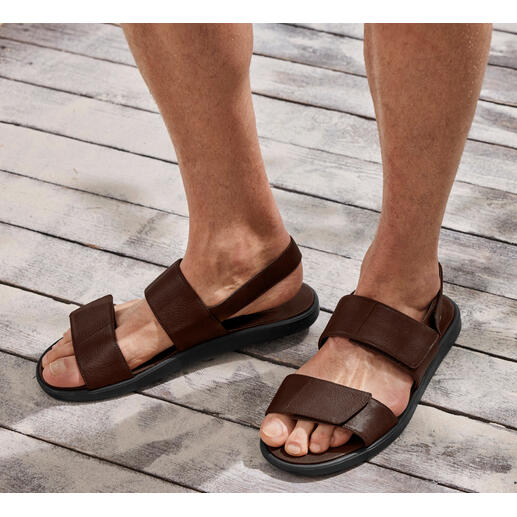 Ultralichte leren sandalen Bruine leren sandaal met twee banden op een voet op een houten vloer.