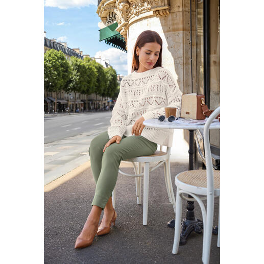Pourchet Paris raffia boxy-bag Vrouw in gebreide trui zit aan een tafel met een kop koffie en een tas, met een stad op de achtergrond.