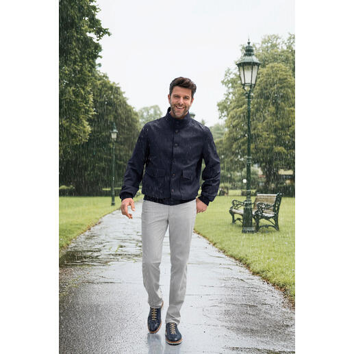 Storm-System®-blouson Man in Storm-System®-blouson wandelt in de regen over een geplaveide weg in een park.