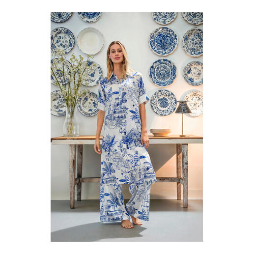 blousejurkje en broek met wijde pijpen Vrouw in Esisto zijden stretchcombinatie staat voor een muur met blauwe borden.