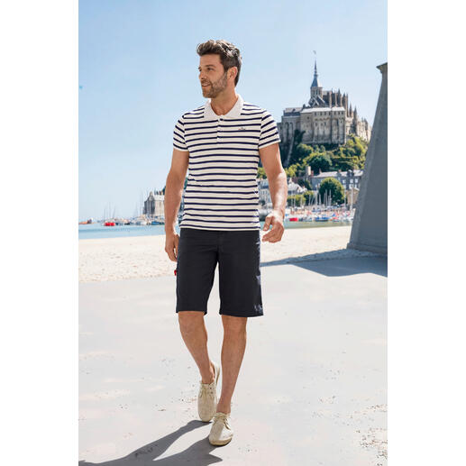 Saint James Bretons poloshirt Man in gestreept Saint James Bretagne Poloshirt, wandelend op het strand.