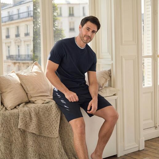 Man zit in een kamer en draagt een marineblauwe recovery-pyjama met korte mouwen.