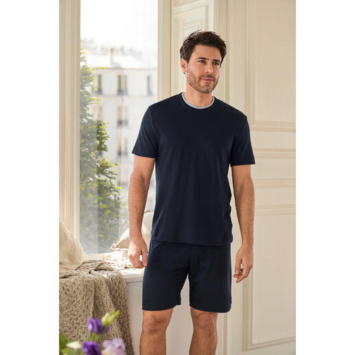 Recovery-pyjama Man staat in een lichte kamer in een marineblauwe recovery-pyjama met korte broek.