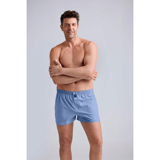 lichtblauw Man in blauwe comfort boxershorts staat glimlachend voor een neutrale achtergrond.