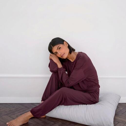 Vrouw zit op een kussen in een paarse loungewear shirt en broek.