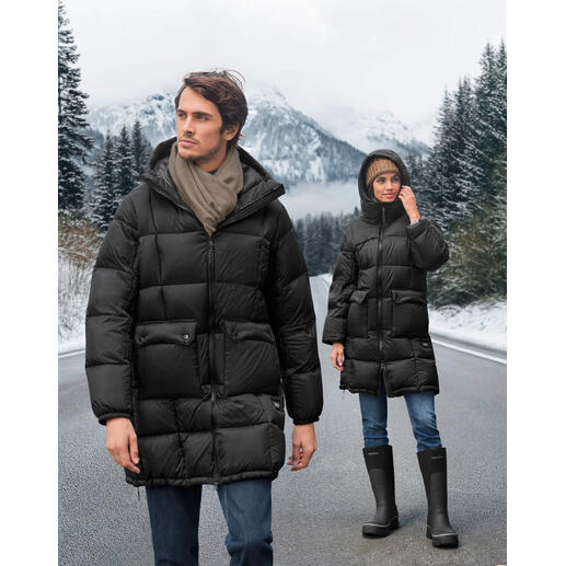 Twee personen in zwarte dons parka op een winterse weg met bergen op de achtergrond.