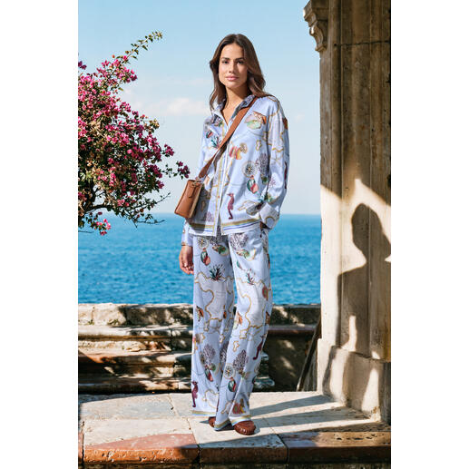 Vrouw in zijde pyjama met kleurrijk bloemenpatroon aan zee.