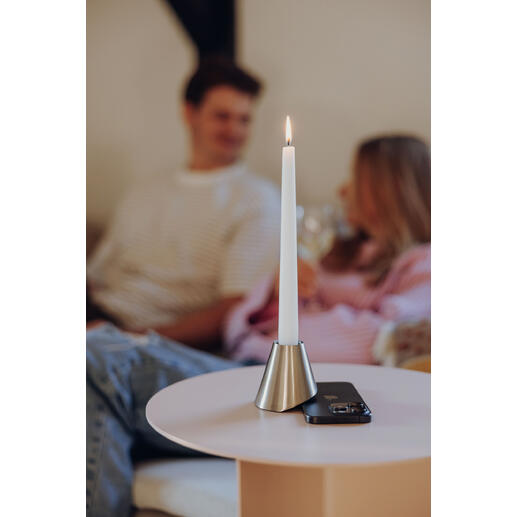 Kaars in metalen houder op tafel, achtergrond met mensen.