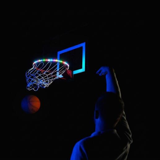 Basketbalnet met kleurrijke LED-lampen en persoon die gooit op een donkere plek.