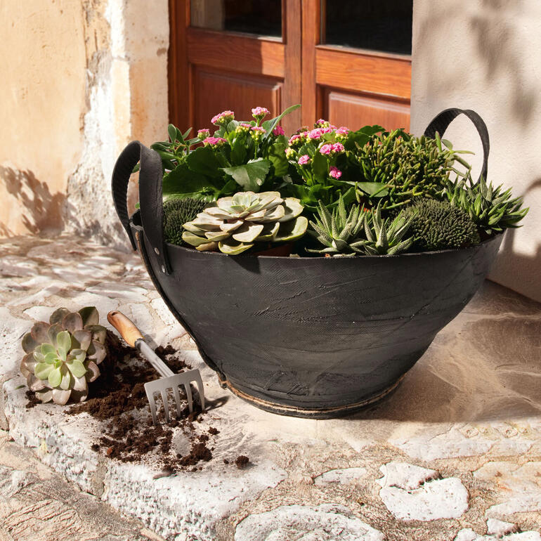 Mand van vrachtwagenbanden met kleurrijke planten, decoratief en duurzaam op een stenen oppervlak.